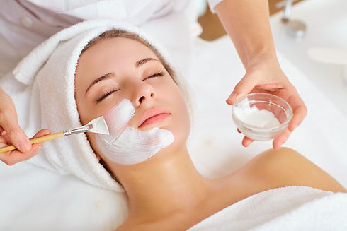 This is an alt text of a relaxed woman with her hair in a towel getting a facial applied by an esthetician.